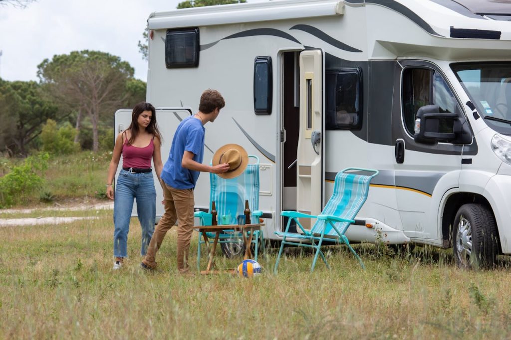 Outdoor scene of a young couple setting up camp next to their RV during a summer day in Portugal.